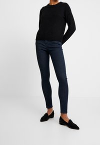 Svart stickad tröja med rund halsringning, i kombination med mörkblå smala jeans och svarta slip-on loafers, med en slät yta och figurnära design.