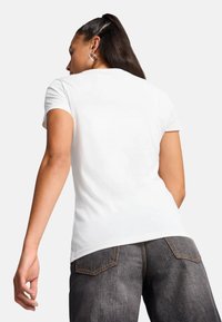 Hvid, tætsiddende t-shirt med korte ærmer, der har en glat tekstur. Modellen har mørke jeans på med et klassisk femlomme-design.