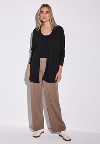 Svart, lätt cardigan med öppen framsida, kombinerad med beigefärgade vida byxor och vita sneakers, lämplig för avslappnade miljöer.