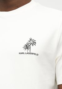 Λευκό T-shirt με μαύρο γραφικό φοίνικα πάνω από το κείμενο "KARL LAGERFELD" που είναι τυπωμένο στο αριστερό στήθος.