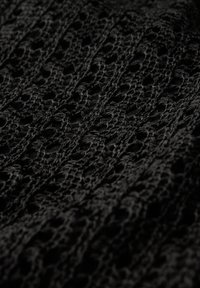 Tessuto nero lavorato a maglia con un motivo aperto simile a pizzo. Superficie testurizzata che mette in evidenza intricati occhielli. Aspetto leggero e traspirante.