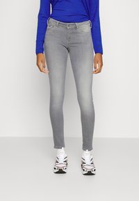 Šedé skinny džíny s hladkým povrchem a jemným vyblednutím, kombinované s modrým topem s dlouhým rukávem a vzorovanými teniskami.