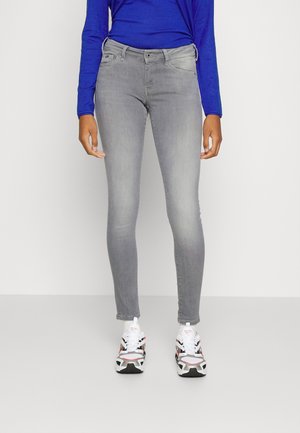 Jeans skinny grises con una textura suave y un desvanecimiento sutil, combinados con una camiseta de manga larga azul y zapatillas con estampado.