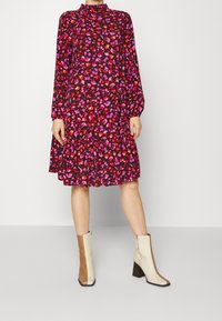 Kwiatowa czarna sukienka z długimi rękawami i wysokim dekoltem, zdobiona wielokolorowymi wzorami kwiatów oraz rozkloszowanym dołem. Grube beżowo-brązowe botki.