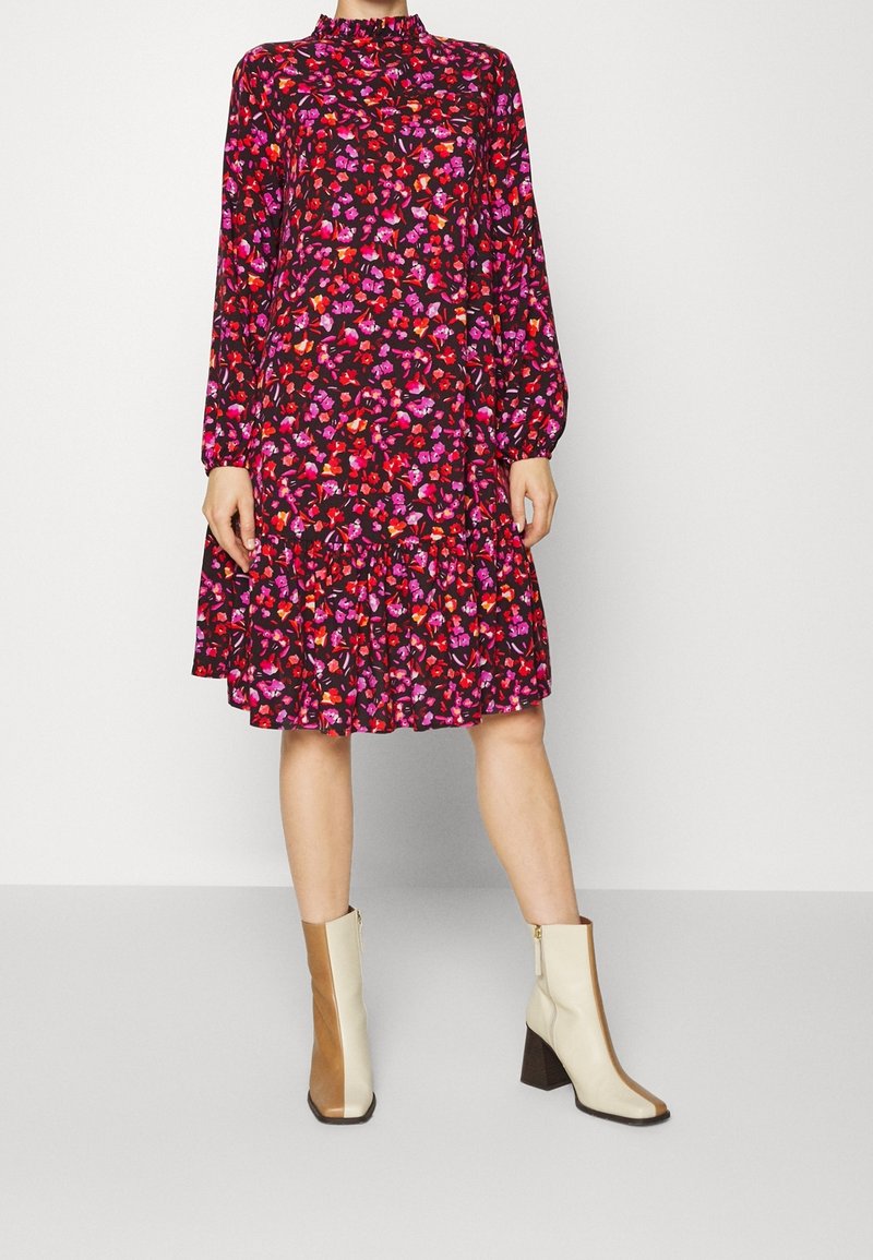 Kwiatowa czarna sukienka z długimi rękawami i wysokim dekoltem, zdobiona wielokolorowymi wzorami kwiatów oraz rozkloszowanym dołem. Grube beżowo-brązowe botki.