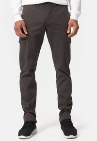 Cargo pants in dark grey fabric with a slim fit, featuring side pockets and subtle stitching details. Worn with black athletic shoes.