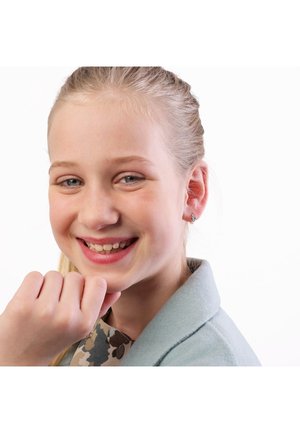 Fille souriante portant un manteau bleu clair avec un col texturé et de petites boucles d'oreilles, affichant une peau claire et de longs cheveux blonds.