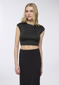 Crop top nero con maniche corte, realizzato in materiale lucido. Texture liscia, abbinato a una gonna nera coordinata. Design minimalista.