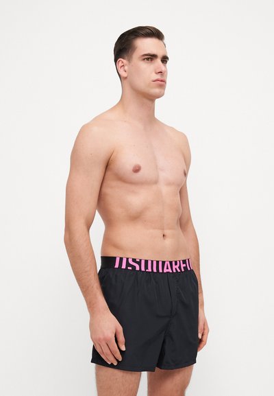 Schwarze Badehose mit einem dicken pinken Bund, der den Text "IS WONDERFUL" zeigt. Die Shorts haben eine lockere Passform und eine glatte Textur.
