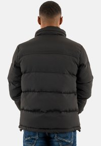 Veste matelassée noire avec sections cousues horizontalement, col haut et poches zippées. Présente une texture lisse et brillante et un ourlet ajustable.