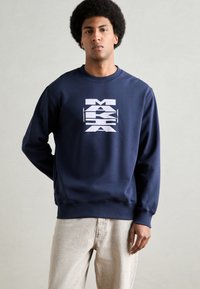 Sudadera azul marino con un estampado gráfico en blanco. Presenta un cuello redondo y puños y dobladillo acanalados. Hecha de una tela suave.