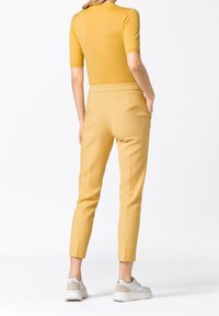 Žlutý upnutý top s krátkým rukávem, zkombinovaný se vzorovanými žlutými kalhotami a bílými teniskami. Viditelné kapsy na kalhotách.
