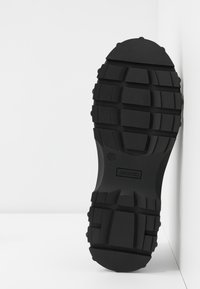 Semelle de chaussure noire avec des crampons profonds, taille 37, et le logo "MONKI" visible au centre, photographiée sur un fond blanc.