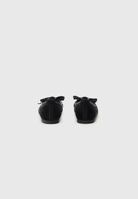 Ballerines plates en suédine noire avec un bout rond, dotées d'un nœud décoratif à l'avant et d'une semelle en caoutchouc plate. Design minimaliste et texture douce.