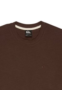 Brązowy t-shirt z okrągłym dekoltem, z małym wszytym logo na lewej piersi i czarną metką wewnątrz kołnierzyka.