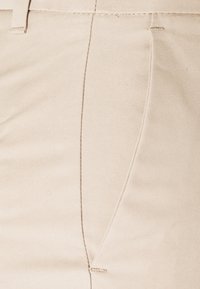 Pantaloni in tessuto beige con una superficie liscia, caratterizzati da un sottile motivo rigato diagonale e cuciture ordinate lungo le cuciture.