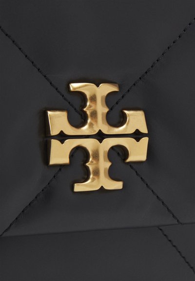 Borsa a mano in pelle nera con un prominente emblema dorato al centro, cuciture dettagliate visibili sulla superficie.