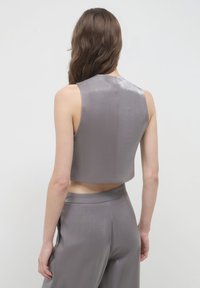 Top court sans manches en tissu gris brillant avec une texture lisse, associé à un pantalon large gris assorti avec une taille simple.