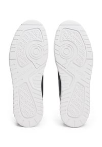 Białe gumowe podeszwy sneakersów z teksturowanymi wzorami antypoślizgowymi; logo widoczne na jednej podeszwie. Gładki czarny materiał na górnej stronie.