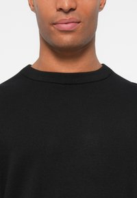 Suéter preto de gola redonda, em material de malha macia com uma textura suave. Design simples, sem padrões ou detalhes visíveis. Vista em close-up.