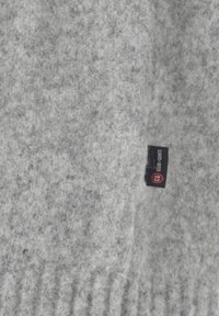 Hellgrauer strukturierter Strickstoff mit einem kleinen schwarzen Etikett, auf dem "CG CLUB GENTS" in weißem und rotem Text angezeigt wird.