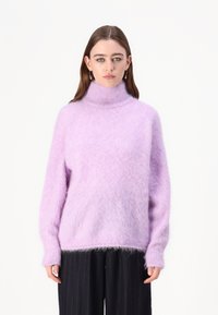 Svetlo vijoličasta oversized pulover s turtleneck ovratnikom, izdelan iz puhastega materiala. Ima dolge rokave in rebrast ovratnik. Mehka, teksturirana izbira.