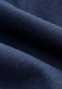 Marineblaue Stoff mit einer weichen Textur, der feine gerippte Muster und glatte Falten aufweist, was auf eine elastische Materialzusammensetzung hinweist.