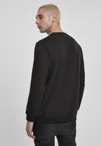 Svart hettegenser med rund hals, lange ermer, ribbestrikkede mansjetter og nederkant. Stoffet ser glatt ut med en ensfarget design og minimalt med detaljer.
