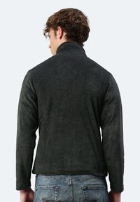 Dunkelgraue Fleecejacke mit hohem Kragen, weicher Textur und langen Ärmeln, rückwärts getragen, kombiniert mit blauen Jeans.