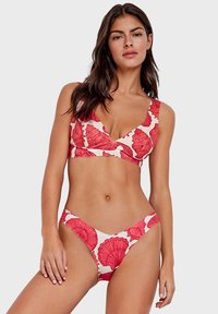 Crveni cvjetni bikini set koji se sastoji od topa s širokim naramenicama i V-izrezom, uparen s donjim dijelom bikinija s niskim strukom; tkanina ima glatku teksturu.