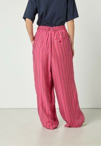 Roze prugaste hlače s opuštenim krojem, elastičnom strukom i bočnim džepovima. Izrađene od lagane tkanine s vertikalnim bijelim linijama.