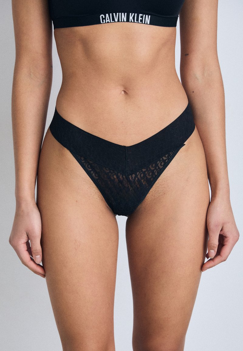 Black lace thong with a V-shaped waistband, featuring a textured pattern and minimal coverage. Soft material for comfort and fit.