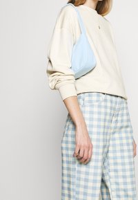 Borsa a spalla azzurro chiaro con una consistenza morbida, abbinata a un sweatshirt color crema e pantaloni a gamba larga a quadri azzurri chiari e gialli.