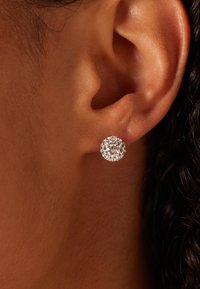 Ronde zilverkleurige studs met meerdere heldere rhinestones, die licht weerspiegelen. Heldere en gestructureerde oppervlakte, geplaatst in een oor.