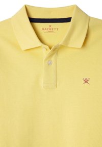 Żółta koszulka polo wykonana z teksturowanej tkaniny. Posiada zapięcie na dwa guziki, granatowy kołnierzyk oraz małe czerwone wyszywane logo na klatce piersiowej.