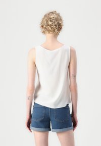 Hvit, ermeløs topp laget av lett stoff, kombinert med rullede denimshorts. Enkel design med buet kant og synlige sømdetaljer.
