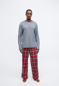 Grå långärmad topp kombinerad med rutiga pyjamasbyxor i rött, svart och creme. Mjukt tyg, avslappnad passform och vida ben.