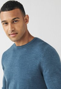 Suéter de punto azul de cuello redondo con una textura suave. Diseño ajustado con detalles acanalados en el cuello y los puños.