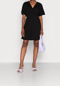 Černé obtažené šaty s krátkým rukávem a elastickým pasem. V kombinaci s levandulovou kabelkou a odpovídajícími sandály na podpatku s pletenými řemínky.