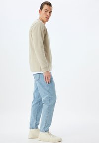 Felpa beige a girocollo abbinata a jeans larghi azzurri e sneakers crema, con uno sfondo bianco semplice.
