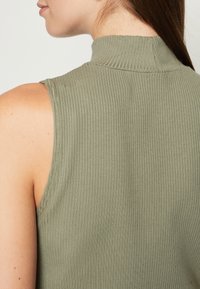 Haut sans manches à col montant en vert olive, fabriqué en tissu côtelé. Présente un design ajusté avec une texture subtile et un décolleté arrondi.