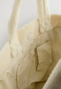 Cremefarvet, fluffy tote bag med blød, struktureret ydre og stofforing. Indvendigt er der en mindre lomme til organisering.