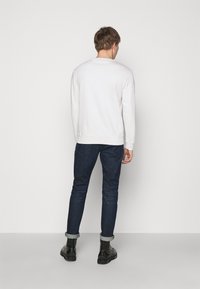 Vit sweatshirt med långa ärmar, rundad halsringning och ribbade manschetter; i kombination med mörka jeans och svarta ankelstövlar; sedd bakifrån.
