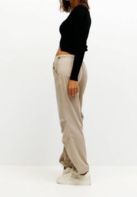 Czarna, długa bluzka crop z długim rękawem w połączeniu z beżowymi spodniami typu wide-leg. Spodnie mają elastyczny pas i boczne kieszenie. Sneakersy w jasnym odcieniu beżu.