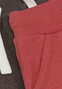 To s�æt stof joggers: ét i mørkebrun med hvide snore, og ét i lys rød med ribbede manchetter og sidelomme.