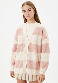 Stickad cardigan med växlande rosa och krämfärgade ränder, V-ringning och knäppning. Den har en avslappnad passform och ribbade ärmslut.