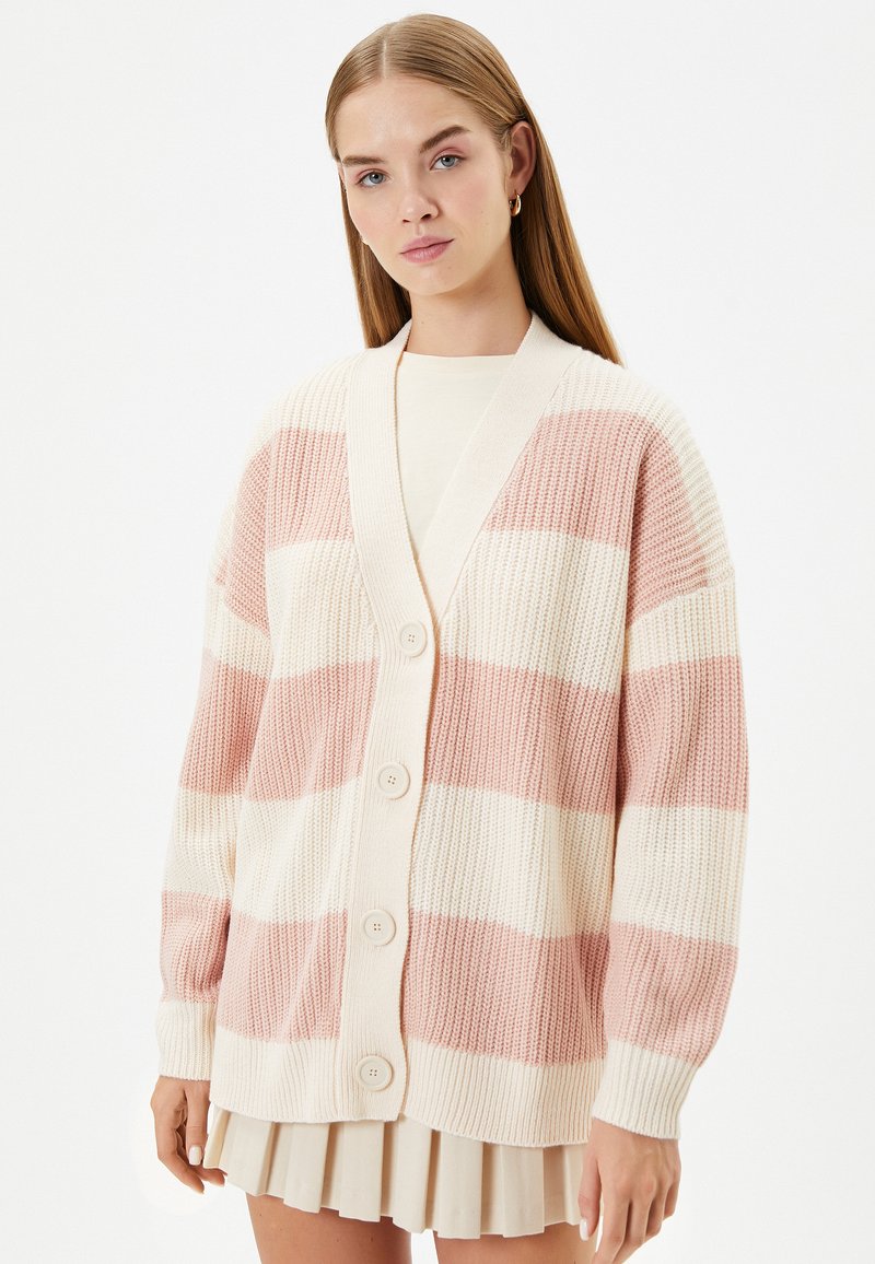 Stickad cardigan med växlande rosa och krämfärgade ränder, V-ringning och knäppning. Den har en avslappnad passform och ribbade ärmslut.