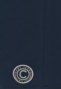 Laivastonsininen ribbineuloskangas, jossa oikeassa alakulmassa pyöreä logo, jossa lukee "CARS JEANS" ja alhaalla "SINCE 1982".