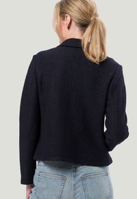 Navy wool jacket with a tailored fit, featuring a notched collar and long sleeves, textured fabric, and a cropped hemline.