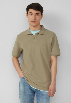 Khakifarbenes Poloshirt mit klassischem Kragen, kurzen Ärmeln und einem dezenten Strukturmuster. Trägt man über einem hellblauen T-Shirt. Legere Passform.